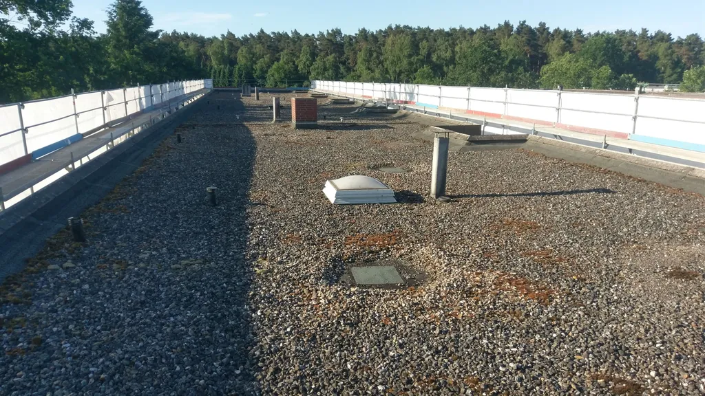 Flachdach mit altem Kiesbelag, Moos und einer Lichtkuppel