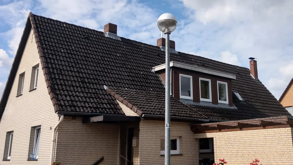 Siedlungshaus mit altem dunklem Dach, brauner Holzgaube und Ziegelkamin